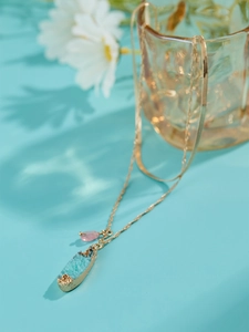 Detail of golden necklace featuring light blue druzy pendant and pink gemstone decoration
