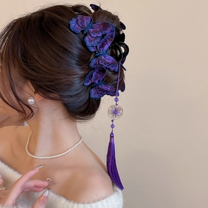 Dettaglio del fermaglio a farfalla ricamata viola con fiore dorato e nappine di seta