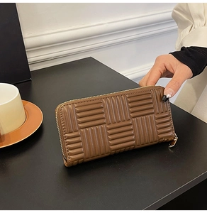 Detail showing brown leather long wallet with woven texture and smooth zipper closure