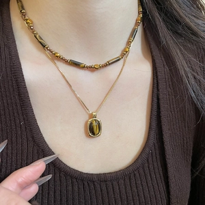 Detail of layered tiger eye stone necklaces on a brown ribbed sweater for women