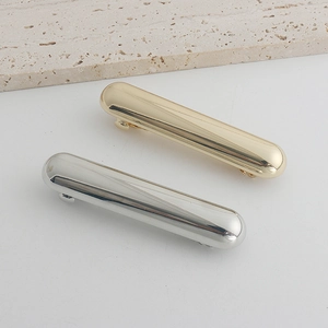 Detail of polished gold and silver capsule-shaped metal hair clips on a stone surface