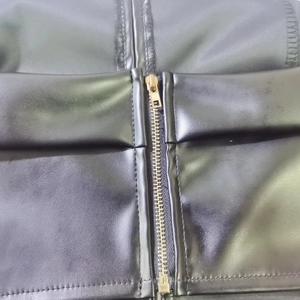 Detailaufnahme der schwarzen PU-Lederstruktur mit hochwertigem goldenem Metallreißverschluss