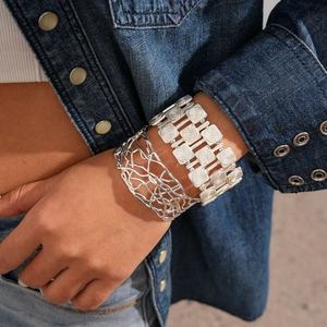 Close-up of geometric textured silver bracelets on model wearing a denim jacket