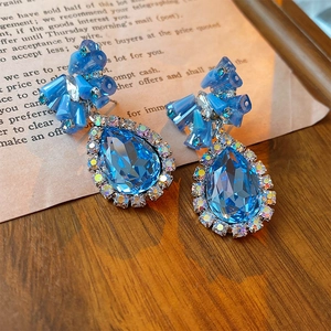 Close-up of blue water-drop crystal earrings with rhinestone bow on a vintage background