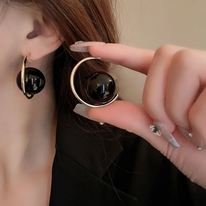 Close-up of a gold C-shape hoop earring with a black bead on a model's ear