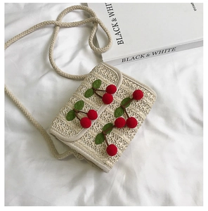 Detail of hand-woven straw crossbody bag featuring 3D plush cherry charms and leaf accents