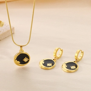Detail of gold necklace and earrings set with black enamel and daisy motifs on beige fabric