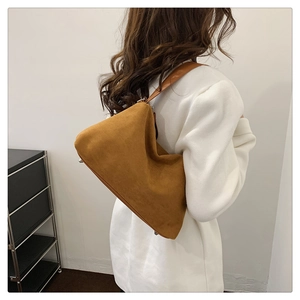Sac hobo en daim marron mat porté à l'épaule par un mannequin au style rétro