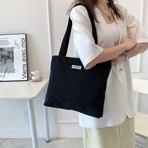 Close-up of black corduroy tote bag featuring soft ribbed texture and FASHION woven label