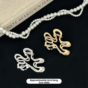 Detail of gold and silver wavy metal hair clips with dimensions 6cm x 3cm on a textured surface