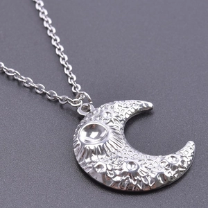 Macro view of silver moon pendant with embossed sun and star textures on steel chain