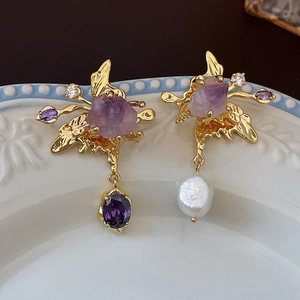 Macro shot of asymmetric gold earrings with amethyst stones and white baroque pearls