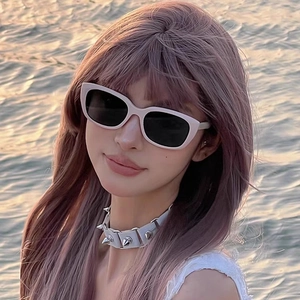 Pink-toned photo of a woman wearing white cat-eye sunglasses and white spiked choker necklace