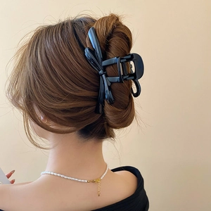 Detail of large black glossy ribbon hair claw clip worn on elegant brown braided hair