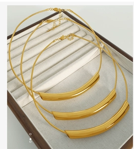 Detailed view of three polished gold snake chains with curved tube pendants on a display