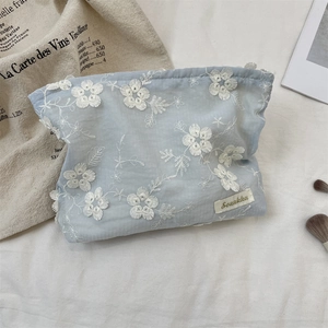 Close-up of light blue fabric makeup bag with white floral embroidery and woven label