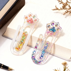 Close-up of sparkling resin cat paw bookmarks with colorful sequins on book pages