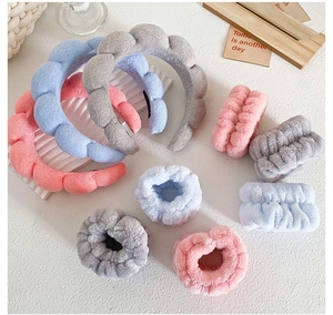 Soft plush spa headband and wristband set in pink, blue and grey displayed on a table