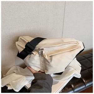 Detail view of cream nylon crossbody bag with wide black strap and dual zip compartments
