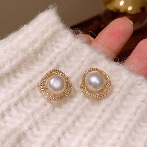 Detail of elegant gold-plated pearl stud earrings with zircon halo on white knit