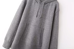 Detailed view of grey knitted hoodie texture featuring drawstring and kangaroo pocket design