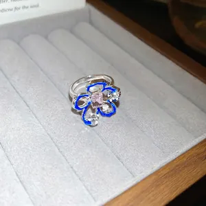 Anello a fiore traforato con smalto blu e pietra rosa su espositore per gioielli in velluto