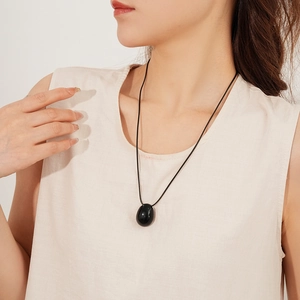 Détail du pendentif ovale noir minimaliste sur cordon de cire porté par un modèle