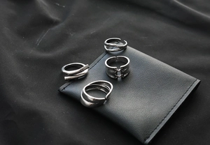Detailed view of four silver minimalist rings featuring chain and woven designs on black leather