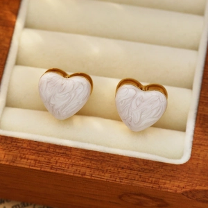 Détail de boucles d'oreilles cœur en marbre blanc avec bordure dorée dans un écrin