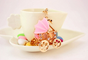 Close-up of golden baby stroller keychain with pink crystals in a heart-shaped dish