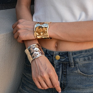 Detail of wide metallic cuff bracelets with irregular wavy texture on model's arms