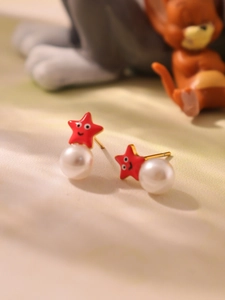 Primer plano de pendientes infantiles bañados en oro con estrella roja y perla blanca