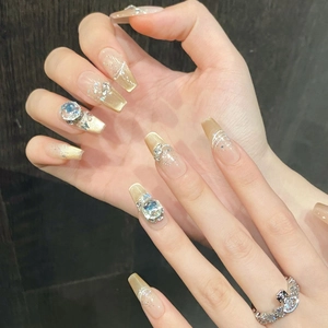 Close-up of nude long coffin press-on nails with gold glitter, heart rhinestones and swirls