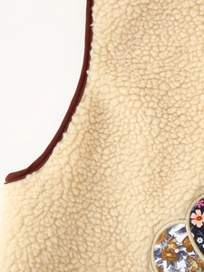 Detailed close-up of beige faux shearling vest fabric with floral patch and brown trim