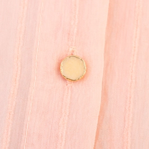 Close-up of pink striped fabric with elegant gold-edged button and soft texture