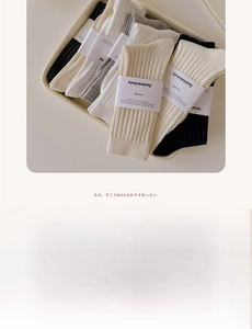 Detail of ribbed cotton mid-calf socks in cream, grey, and black with paper tags
