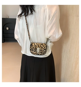 Fashionable leopard print saddle bag with metal buckle worn by model in minimalist setting