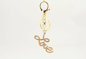 Close-up of golden metal keychain featuring cursive LOVE pendant with sparkling rhinestones