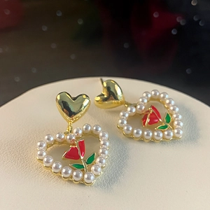 Macro view of heart-shaped gold earrings with red rose, green leaves and pearl accents