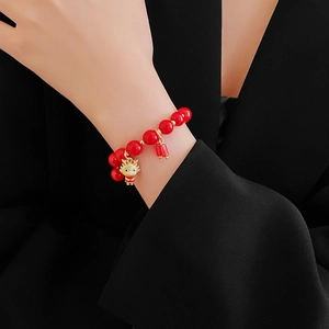 Gros plan d'un bracelet en perles rouges avec pendentif dragon doré porté au poignet