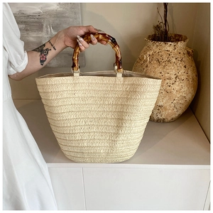Detail view of woven straw tote bag with brown bamboo handles in a natural home setting