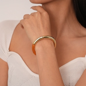 Détail du bracelet géométrique en résine orange et métal doré porté au poignet