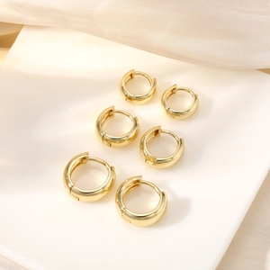 Three pairs of polished gold hoop earrings arranged on a white ceramic plate with silk