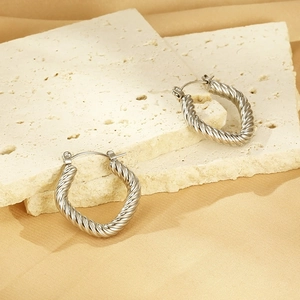 Detailed view of silver twisted cable earrings on neutral textured background