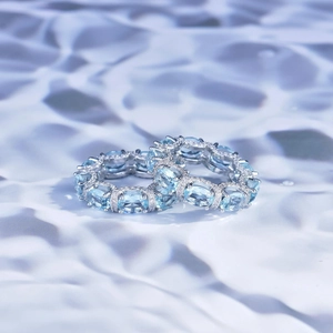 Detail of two silver rings with oval aquamarine stones and pavé set white gems on water ripples