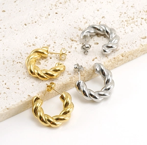 Macro view of gold and silver twisted C-shaped earrings on textured stone surface