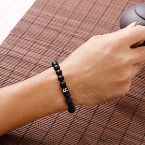 Detail of beaded bracelet with black lava stone and letter R charm on hand