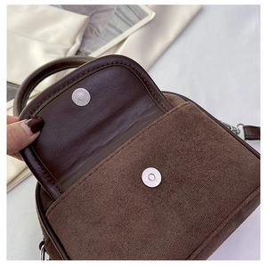 Close-up of dark brown plush handbag with silver magnetic snap and soft suede texture