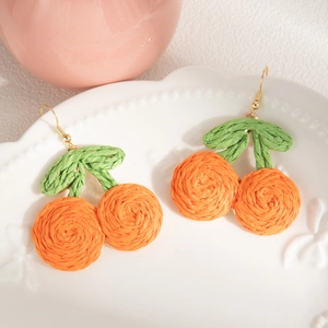 Handmade bohemian woven orange fruit earrings on white plate for beach vacation style