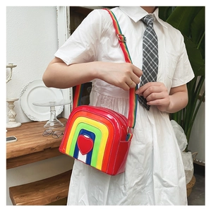 Detail of a rainbow crossbody bag with a glossy 3D red heart and striped fabric strap